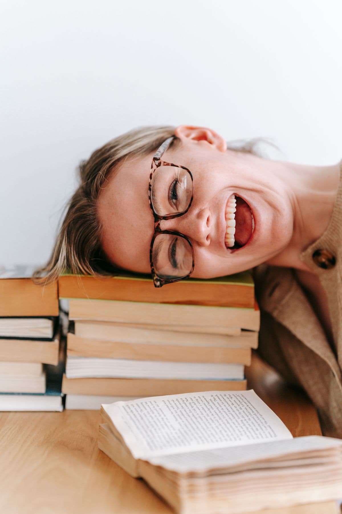 A student laughing with her head resting on a stack of books